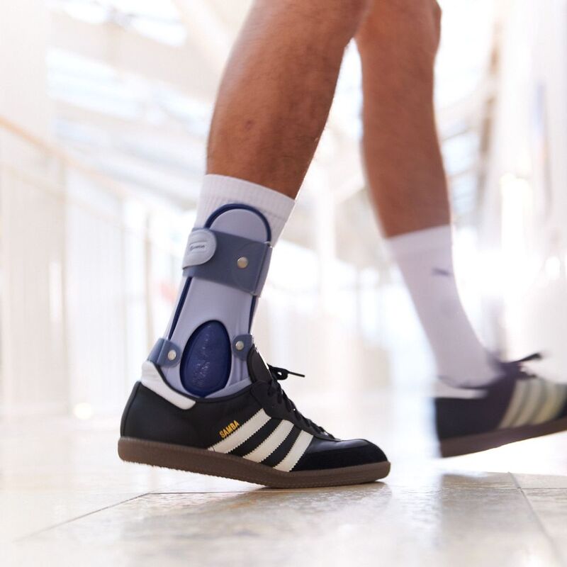 Fits in Shoes Close-up of a person walking with an orthopedic ankle brace and black Adidas Samba sneakers.
