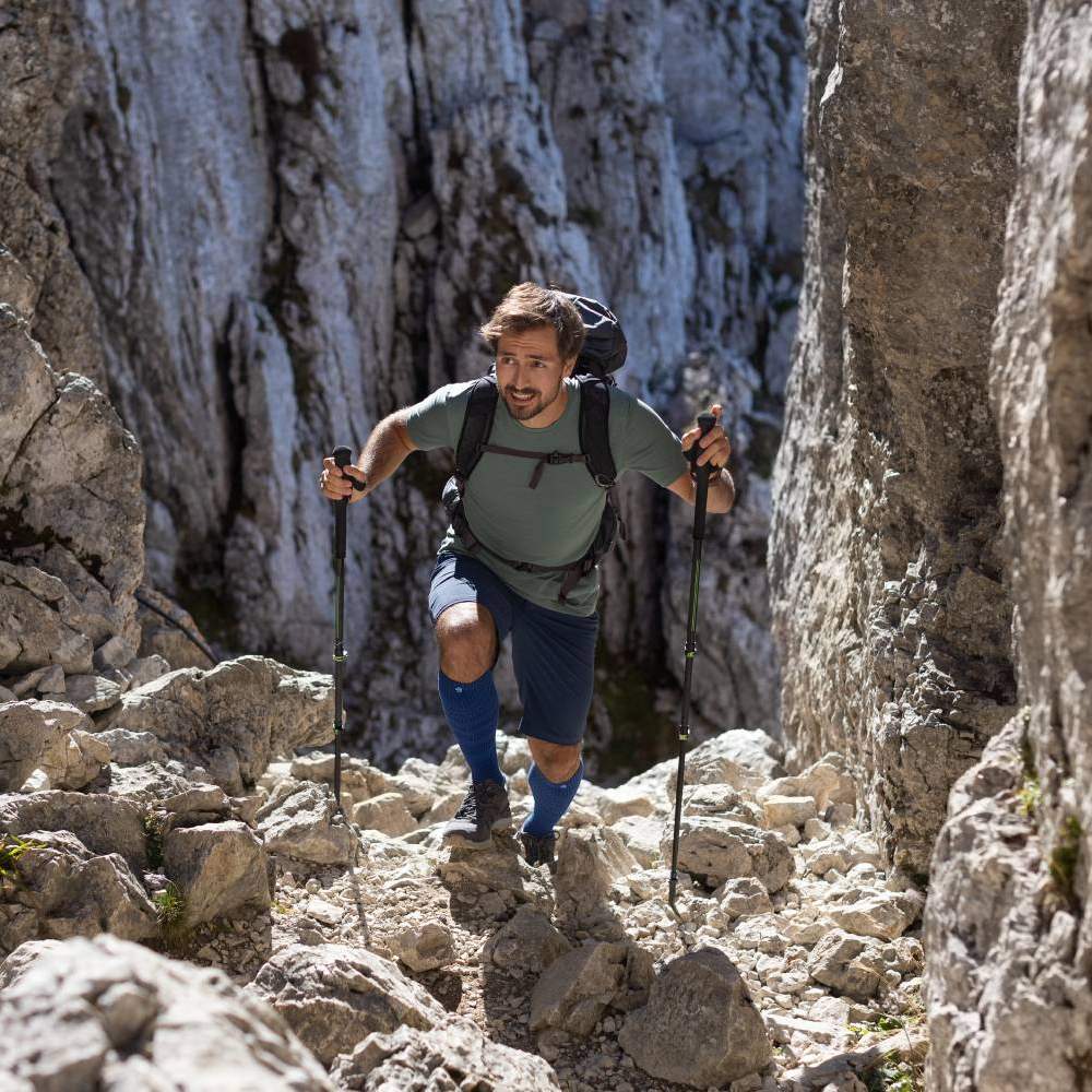 Man hiking in rocky mountain terrain with trekking poles and backpack