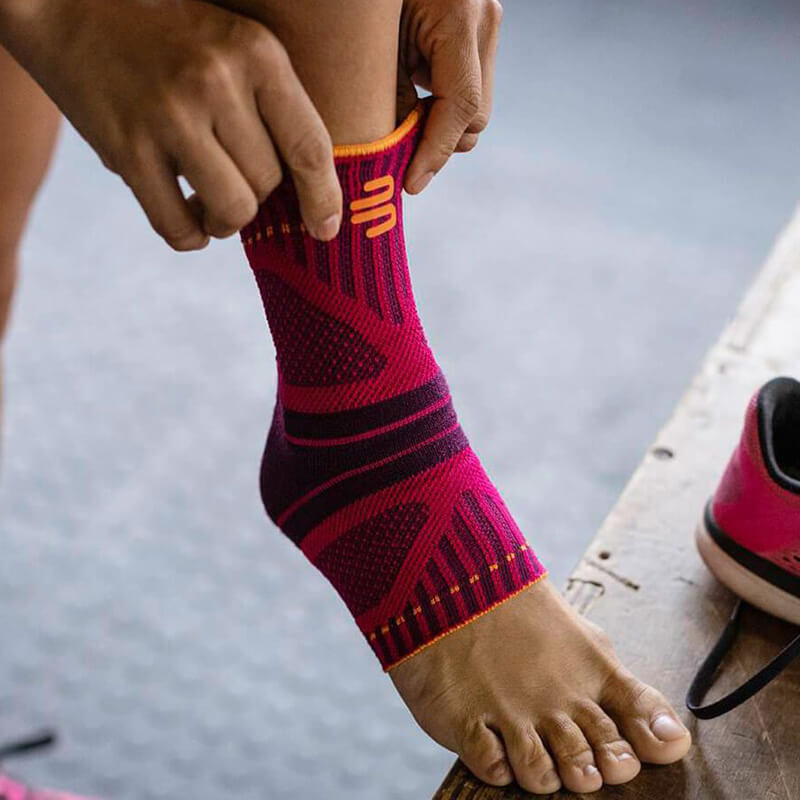 Woman putting on Bauerfeind's Sports Ankle Support Dynamic before beginning her workout at a fitness center.