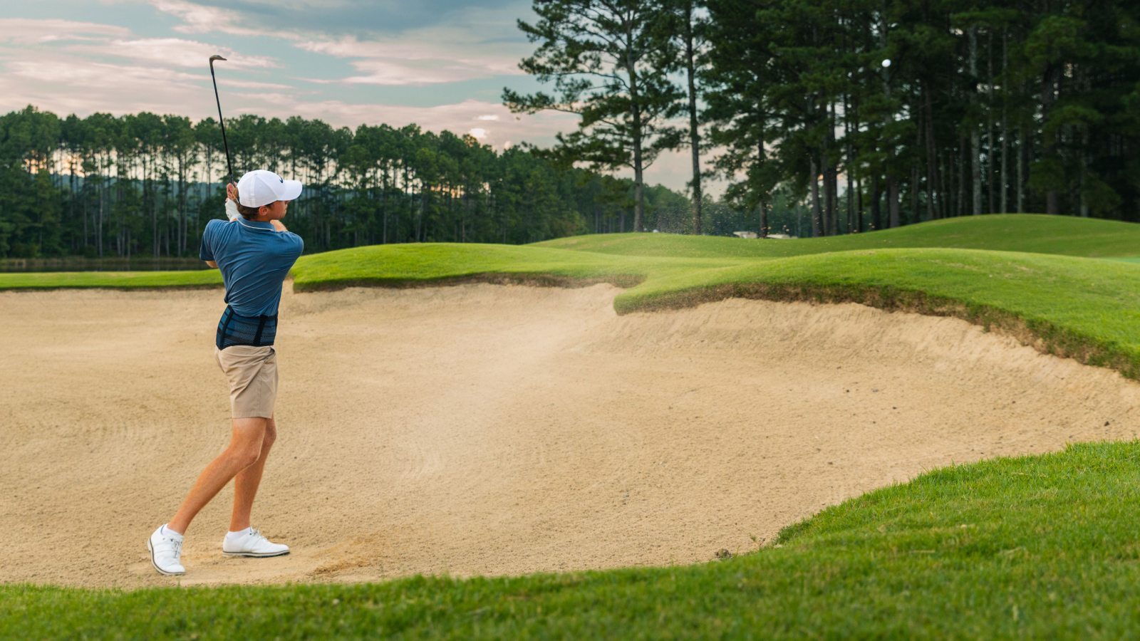 Golfer wearing Bauerfeind's Sports Back Support while hitting out of a sand bunker.