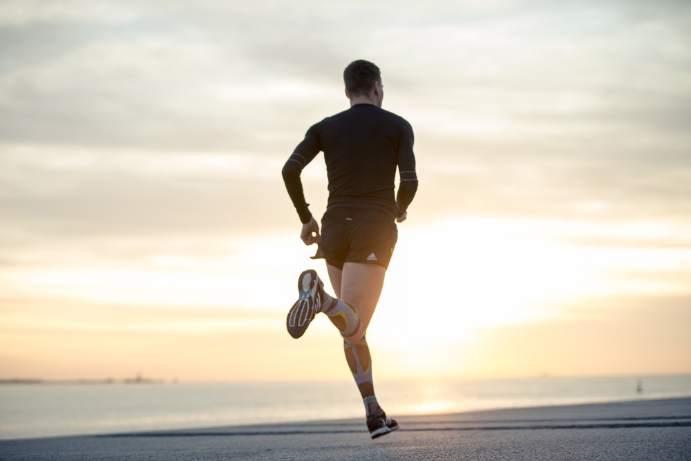 Benefits of Addressing Running Form Man wearing Bauerfeind's Run Performance Compression Socks while running next to the ocean in the morning.