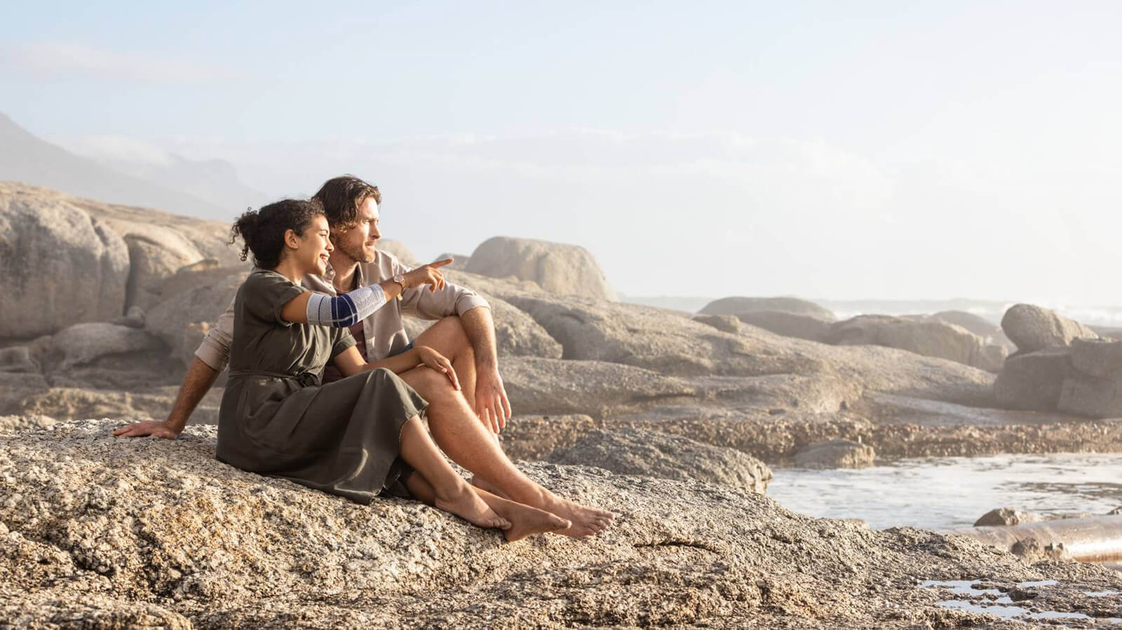 Woman wearing the EpiTrain while sitting with man near the ocean. Couple sitting on rocky coast and pointing towards ocean, with the woman wearing Bauerfeind's EpiTrain elbow brace.