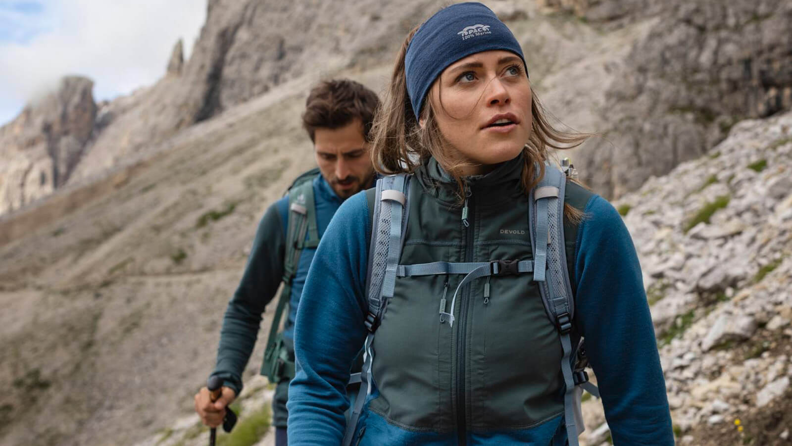 Man and woman hiking through rocky mountain terrain. Young man and woman hiking in rugged mountain terrain, both wearing backpacks and outdoor gear, focused on the trail ahead.