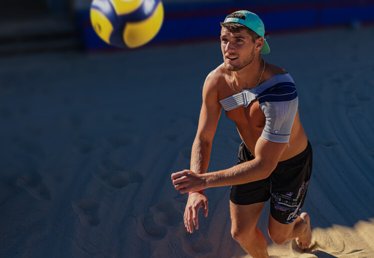 Male athlete competing in beach volleyball while wearing the OmoTrain S. Male athlete competing in beach volleyball while wearing Bauerfeind's OmoTrain S shoulder brace.