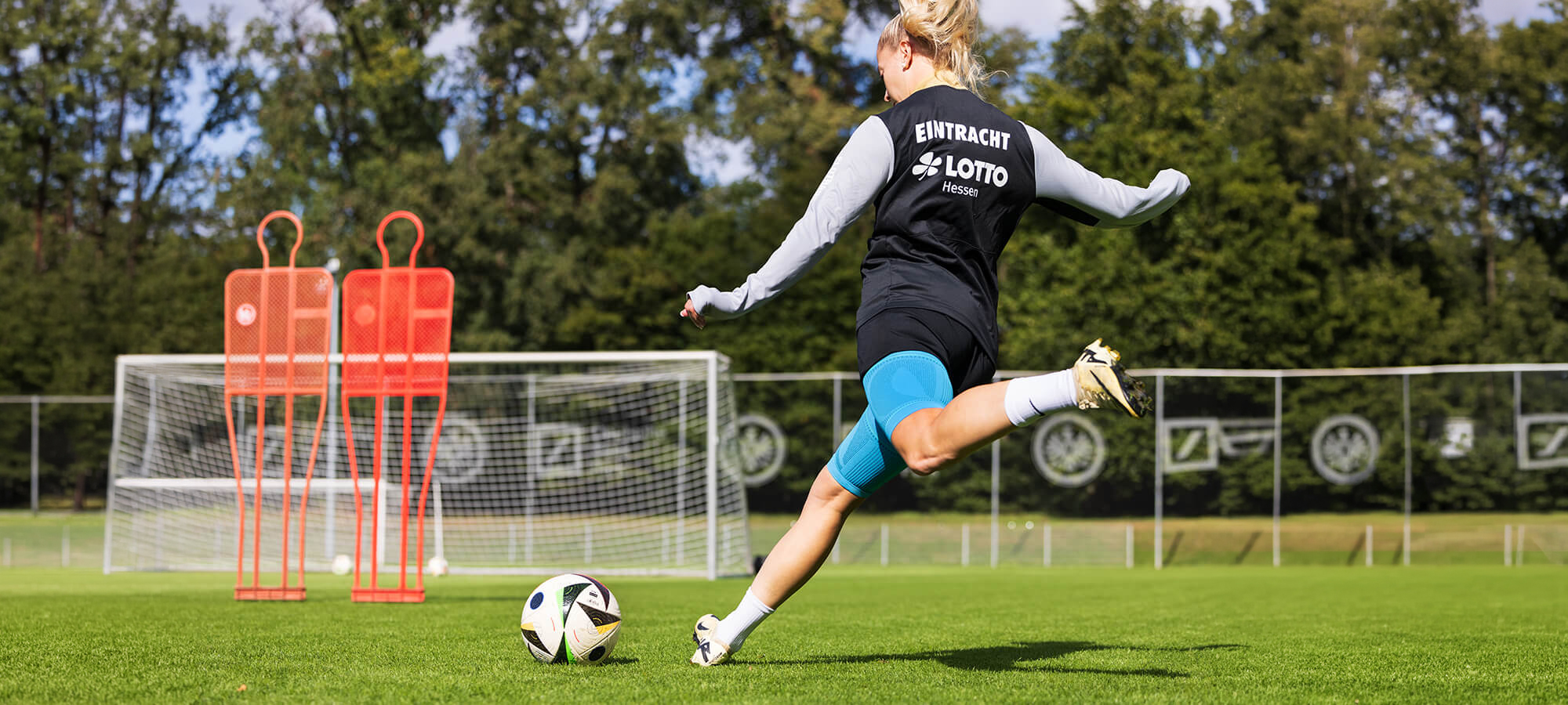 Soccer player wearing Bauerfeind's Sports Compression Upper Leg Sleeves while kicking the ball toward the net.