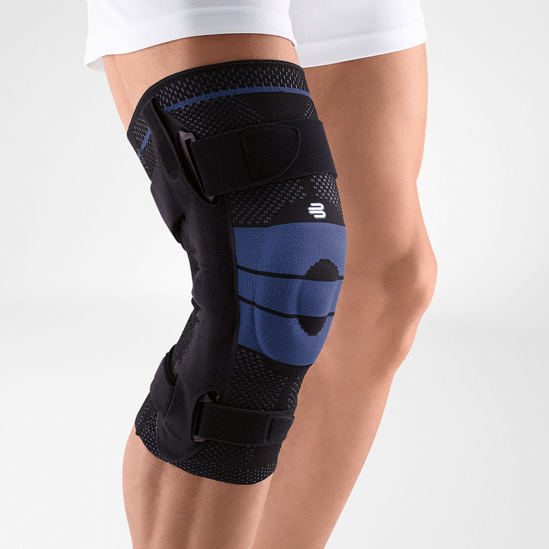 Close-up view of Bauerfeind's black GenuTrain S hinged knee brace on a person's leg, showcasing adjustable straps and knee pad for joint stability and injury recovery.