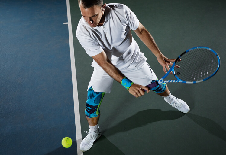 Tennis Player Wearing the Sports Knee Support and Sports Wrist Strap Tennis player wearing Bauerfeind's Sports Knee Support and Sports Wrist Strap while attempting to hit the tennis ball.