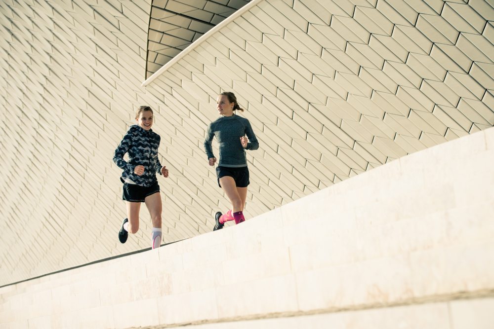 Woman wearing the Run Performance Compression Socks while running through a city street. Woman wearing Bauerfeind's Run Performance Compression Socks while running through a city street.