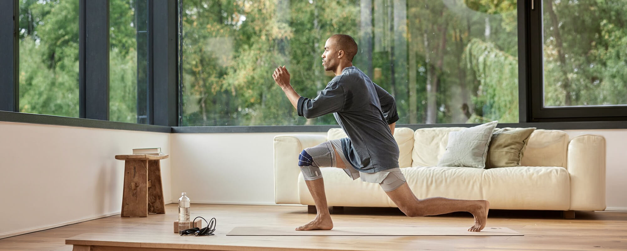 Man performing lunges during an in-home workout while wearing Bauerfeind's GenuTrain knee brace.