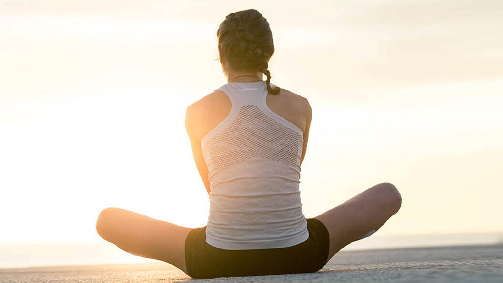 Woman stretching before her morning run by the ocean. Woman performing a seated leg and hip stretch before her morning run by the ocean.