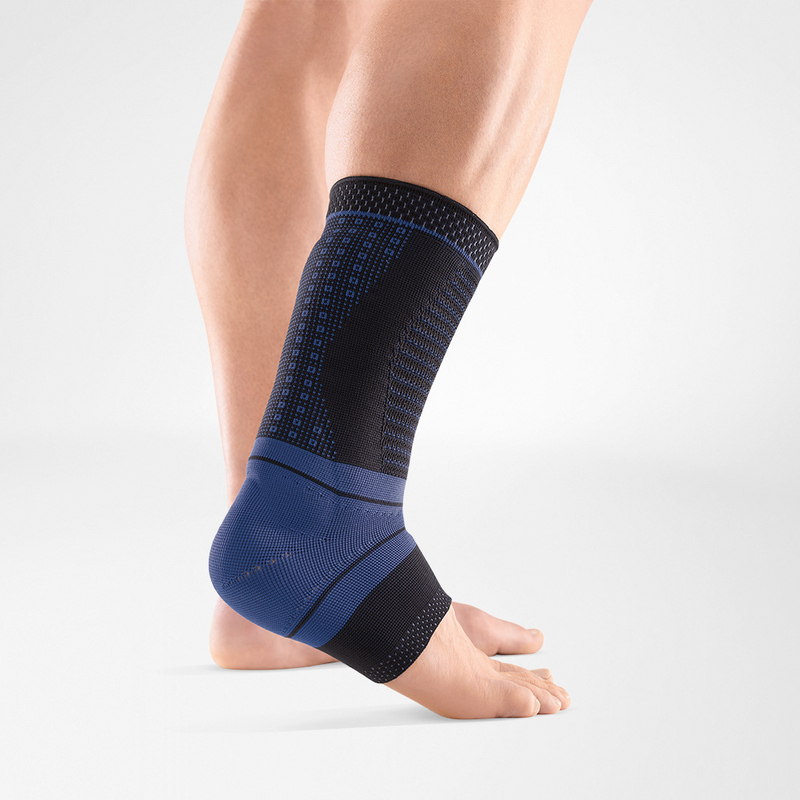 Close-up view of a person wearing a blue compression ankle brace on their left foot, set against a plain light gray background.