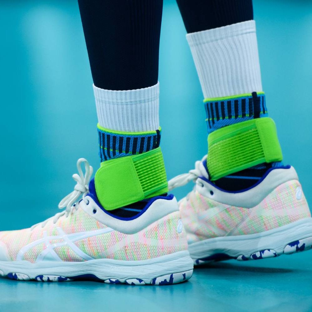 Sport Shoes with Neon Green Ankle Supports on Indoor Court Close-up of a person wearing white sport shoes with neon green ankle supports, on blue indoor court.