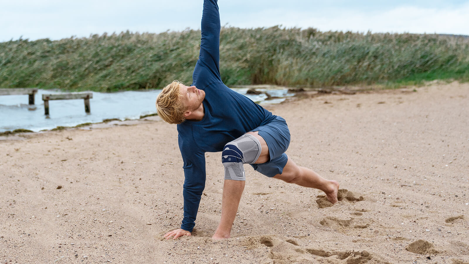 Man practicing yoga on the beach wearing the GenuTrain. Man practicing yoga on the beach wearing Bauerfeind's GenuTrain knee brace.