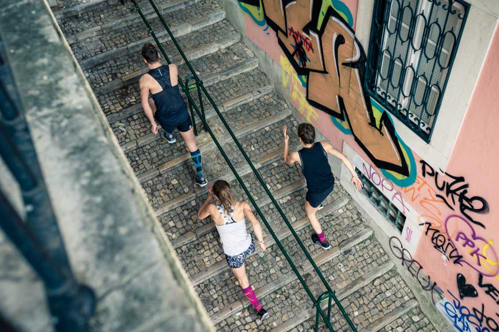 Three young adults wearing the Run Performance Compression Socks while running uphill. Three young adults wearing Bauerfeind's Run Performance Compression Socks while running uphill in an inner-city street.