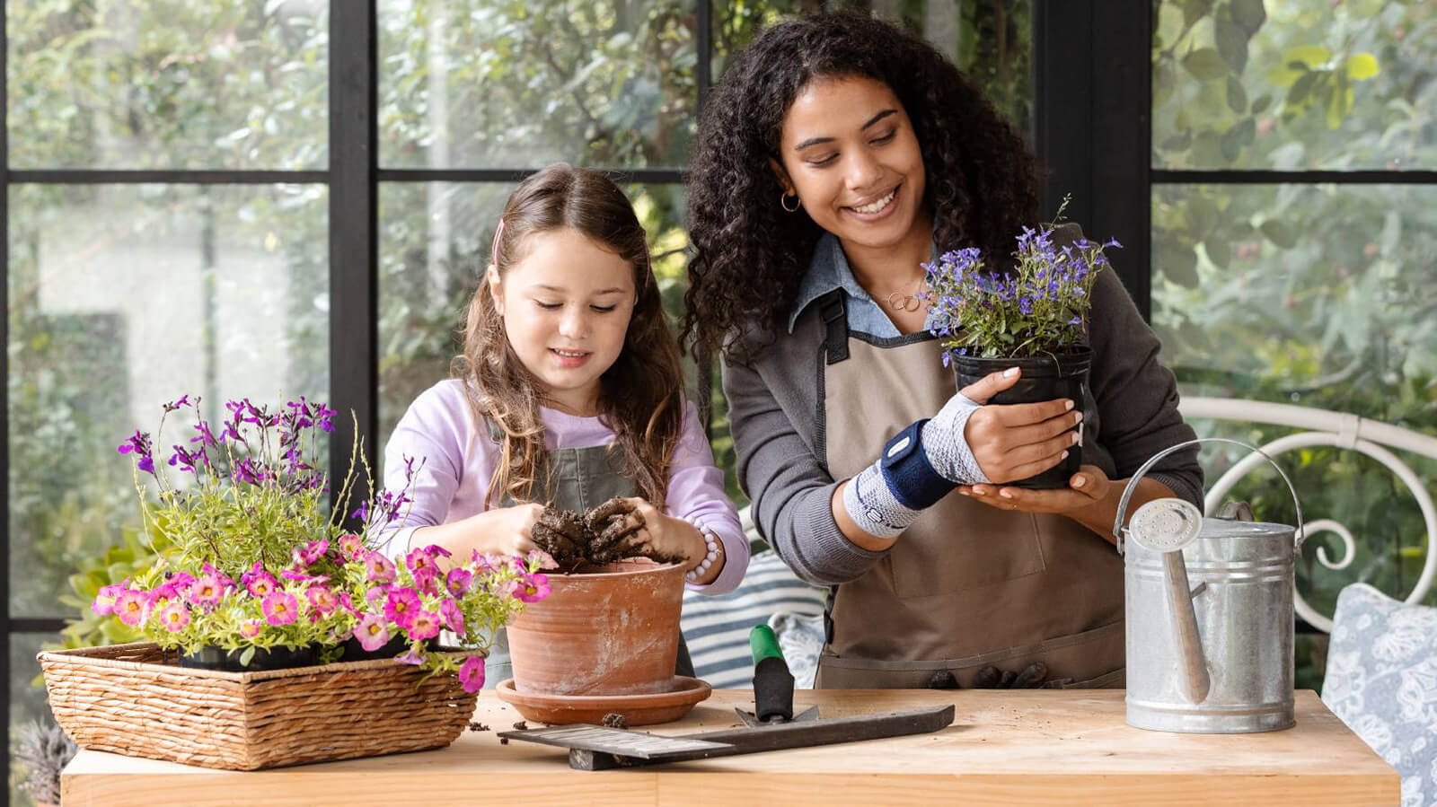 Woman planting flowers with a child while wearing the ManuTrain. Woman planting flowers with a child while wearing Bauerfeind's ManuTrain wrist brace.