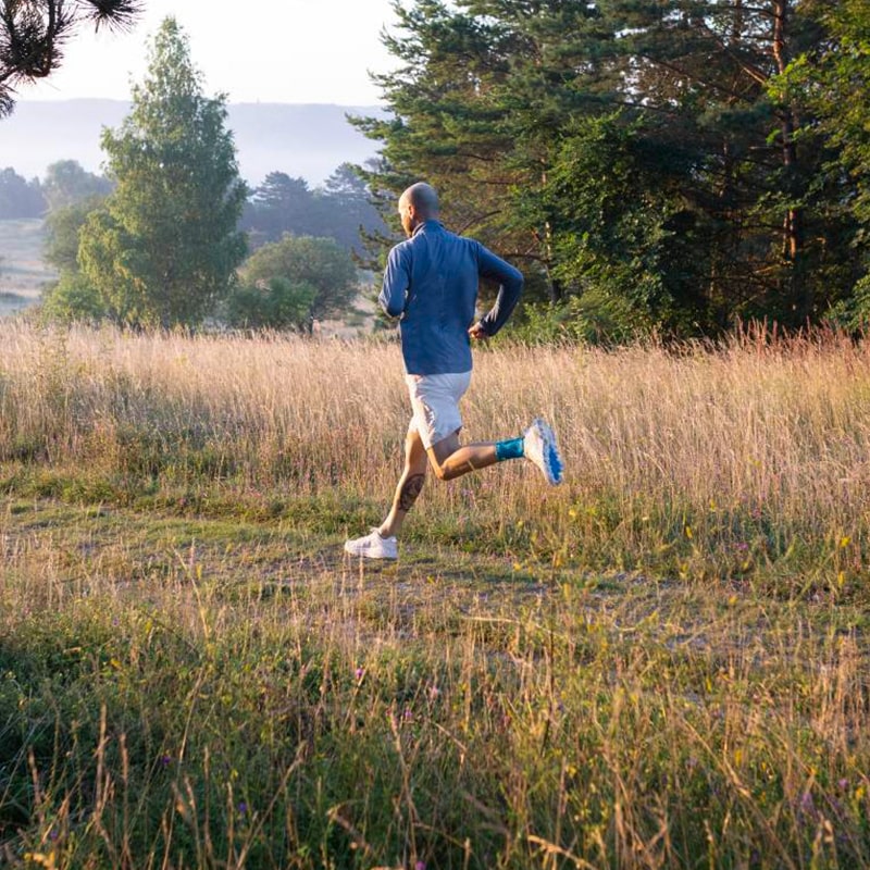 Man wearing the Sports Achilles Support while on a morning run through a grassy field. Man wearing Bauerfeind's Sports Achilles Support while on a morning run through a grassy field.